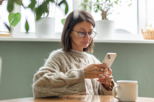 Woman using a smartphone while sitting at a table, related to mobile app development platforms.